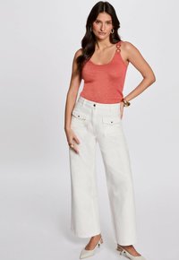Coral glitter tank top with decorative shoulder rings, paired with high-waisted, wide-leg white pants featuring front pockets and gold accents.