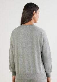 Grå sweatshirt med en afslappet pasform, ribbede manchetter og kant. Har en simpel tekstur og rund hals design, vist fra bagsiden.