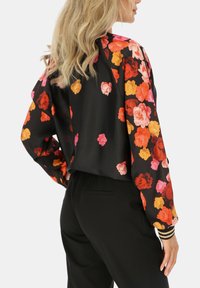 Czarna kurtka z żywym wzorem kwiatowym w kolorze pomarańczowym, różowym i żółtym. Posiada długie rękawy, luźny krój oraz paski na mankietach.