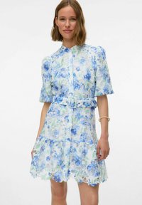Abito in pizzo floreale con motivi di fiori blu e verdi, maniche a palloncino corte, chiusura frontale con bottoni, vita cinchata con una cintura e orlo svasato.