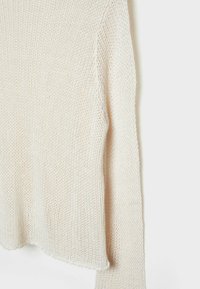 Pull tricoté de couleur crème avec une texture à tissage lâche, montré partiellement avec une manche longue pendante sur un fond uni.