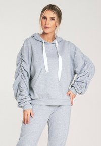 Szara bluza z kapturem, z białymi sznurkami, prążkowanymi mankietami oraz teksturowanymi bufkami na rękawach. Przednia kieszeń typu kangur i luźny fason.