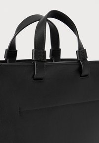 Borsa a tracolla nera in pelle con due manici corti, caratterizzata da una superficie liscia e cuciture ordinate. La borsa ha un design minimalista.