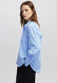 Blauw gestreept overhemd met een relaxte pasvorm, met subtiele geborduurde details en een klassieke kraag. Lange mouwen met knoopmanchetten.