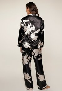 Ensemble de pyjama en satin noir avec de grands motifs floraux beiges. Le haut à manches longues possède un col ; le pantalon est ample avec une coupe décontractée.