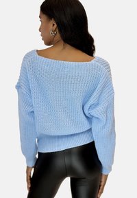 Helles blaues Strickpullover mit weitem Ausschnitt, strukturiertem Stoff, tiefen Schultern und geripptem Saum, kombiniert mit schwarzen Leggings aus Kunstleder.