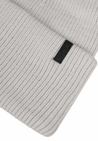 Vaaleanharmaa ribattua neulosta oleva pipo, jossa on käännetty reunus ja pieni musta suorakulmainen kangastarra reunuksessa.