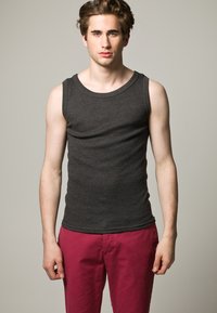 Hall grii ribidega tank top, millel on avar kaelus. Mudel kannab seda kontrastsete roosa värvi pükstega. Kangas näeb välja pehme ja tal on keha lähedane lõige.