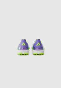 Des chaussures de sport violettes et vertes avec une tige texturée, une semelle intermédiaire blanche et une semelle en caoutchouc verte comportant plusieurs crampons pour l'adhérence.