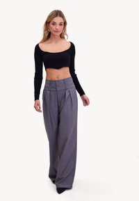 Zwart geribbeld crop top gecombineerd met hoge taille, grijze wijde broek met plooien en een gedetailleerde tailleband. Soepele textuur en op maat gemaakte pasvorm.