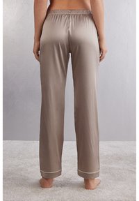 Beige satijnen pyjamabroek met een elastische tailleband, recht model en contrasterende afwerking aan de zoom, gezien vanuit de achterzijde.