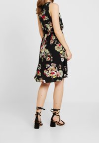 Kwiatowa sukienka na czarnym tle, bez rękawów, z wcięciem w talii oraz zwiewnym dołem. Połączona z czarnymi sandałami na obcasie z wiązaniami w kostce.