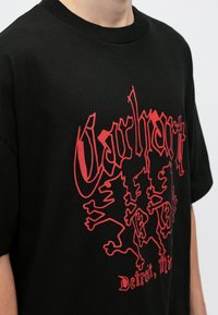Czarna bawełniana koszulka z krótkim rękawem, z wyraźnym czerwonym graficznym wzorem przedstawiającym stylizowane logo i lwy. Projekt z okrągłym dekoltem.