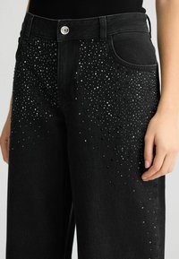 Jeans in denim nero con decorazioni di strass disperse sul davanti, con vita alta e classico design a cinque tasche.