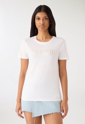Biała bawełniana koszulka z złotym nadrukiem "AMORE" na przodzie, z klasycznym okrągłym dekoltem i krótkimi rękawami, zestawiona z dżinsową spódnicą.