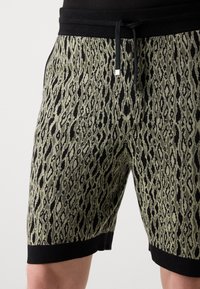 Shorts en maille avec imprimé léopard olive et noir, taille noire avec cordon de serrage, et détail d'ourlet noir.