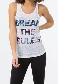 Camiseta sin mangas blanca con textura translúcida, con el texto "BREAK THE RULES" en letras de degradado colorido. Combinada con leggings negros.