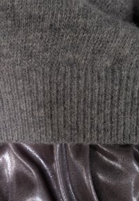 Orlo grigio in maglia di lana con texture a coste, abbinato a un tessuto lucido di un grigio scuro sottostante, che mostra morbide pieghe e lucentezza.