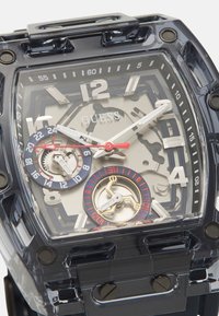 Transparente schwarze Uhr mit rechteckigem Gehäuse. Verfügt über silberne Zifferblätter, rote Akzente und ein strukturiertes Armband. Deutliche Unterzifferblätter sichtbar.