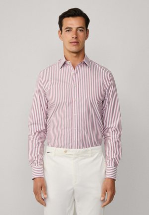 Camisa de botones a rayas en rojo y blanco, de manga larga, con un cuello clásico y un corte entallado, combinada con pantalones blancos.