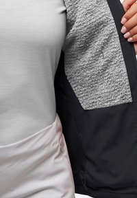 Giacca nera con un interno foderato in pile grigio, una texture esterna liscia e una parte superiore grigia chiara con un design aderente e una leggera lucentezza.