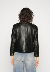 Černá kožená bunda s hladkou texturou, se střihem na míru a zapínáním na knoflíky, v kombinaci s opranými světle modrými džíny.