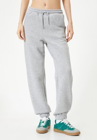 Grijze sweatpants met een elastische tailleband en boorden, met zijzakken. Gepaard met blauwgroene en grijze sneakers met witte veters.