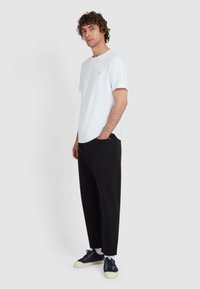 Weißes T-Shirt mit kurzen Ärmeln und rundem Ausschnitt, kombiniert mit schwarzen, locker sitzenden Hosen und marineblauen Sneakers mit weißen Sohlen.