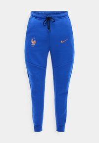 Μπλε αθλητικές φόρμες με μαύρο κορδόνι, που φέρουν πορτοκαλί λογότυπο Nike και έμβλημα κόκορα της Γαλλικής Ποδοσφαιρικής Ομοσπονδίας με δύο αστέρια.