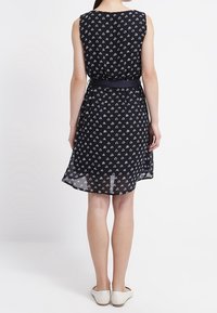 Svart klänning med vitt triangelmönster, utan ärmar, bältad i midjan, lager av tyg, knälång, slät textur och lätt glans.