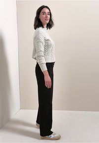 Jasnoszary sweter w splot kablowy, czarne spodnie o prostym kroju oraz szare trampki z jasnoniebieskimi akcentami. Ustawiony na tle neutralnym.