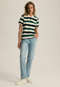 Zielona i biała koszulka polo w paski z zasuwanym kołnierzykiem, zestawiona z jasnoniebieskimi dżinsami o prostym kroju i białymi trampkami. Prosty fason i swobodny krój.