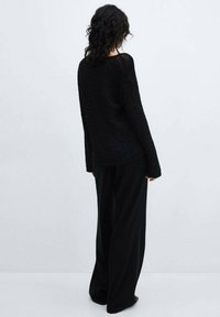 Černý pletený svetr s volným střihem, dlouhými rukávy a texturovanou tkaninou. V kombinaci s širokými černými kalhotami.