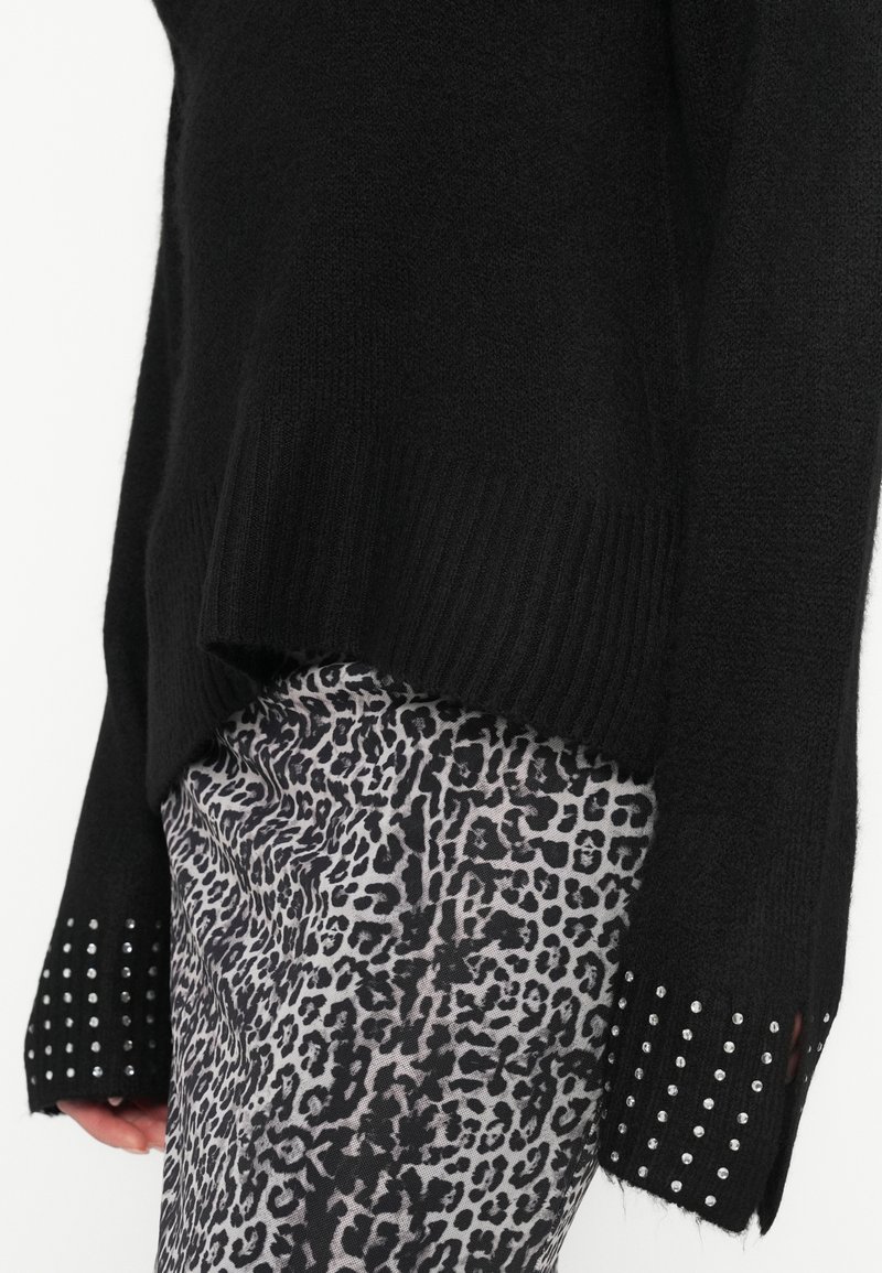 Maglione nero a maglia con polsini a coste, decorato con borchie argentate, abbinato a pantaloni grigi a stampa leopardata. Il design presenta una vestibilità rilassata e una finitura testurizzata.