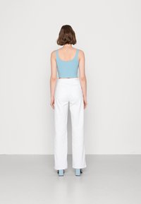 Top corto a righe blu chiaro con spalline larghe abbinato a pantaloni larghi bianchi e scarpe blu con tacco bloccato, visto da dietro.