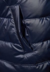 Tkanina granatowej kurtki puchowej z przeszywanymi sekcjami. Charakteryzuje się dużym otworem kieszeni, gładką teksturą i lekką izolacją.