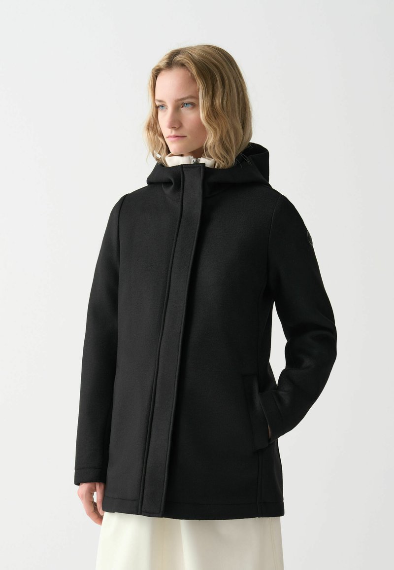 Juodas gobtuvą turintis paltas su tiesiu kirpimu, su priekiniais užtrauktukais, šoninėmis kišenėmis ir tekstūruota medžiaga. Vidus pamuštas šviesios spalvos.