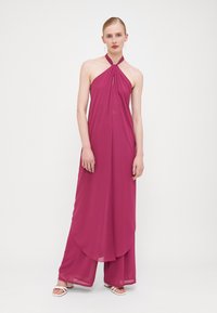 Combinaison à col halter en polyester fuchsia, dotée d'un design fluide avec une texture douce, de pantalons larges et d'un détail en clé à l'encolure.