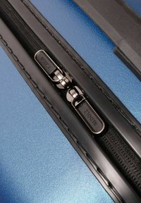 Close-up van een blauwe koffer met twee zwarte ritslussen met het label "REDOLZ" op een zwarte rits.