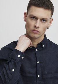 Camisa de botones azul marino en tejido texturizado, con un cuello clásico, botones blancos y un pequeño logotipo bordado en el pecho.