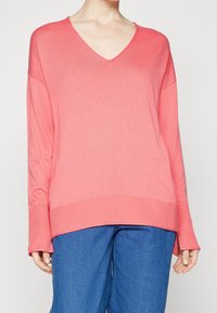 Suéter de punto en coral con cuello en V y puños y dobladillo acanalados. Material suave, corte holgado, hombros caídos. Combinado con pantalones de pierna ancha en azul.