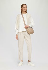 Lichtgewicht beige sweater over een wit shirt, gecombineerd met cremekleurige broek en witte sneakers. Schoudertas in zacht beige.