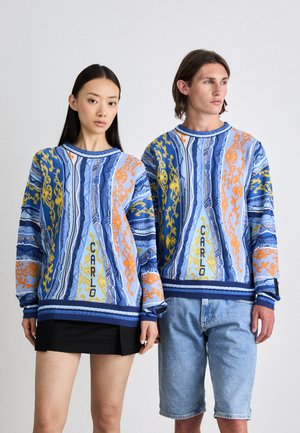 Sweatshirts colorés à motifs aux designs bleu, orange et jaune, avec des poignets et des encolures côtelés, portés par deux personnes.