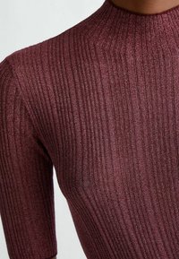 Burgundinpunainen ribbineulottu paita, jossa on korkea kaulus ja lyhyet hihat. Materiaalissa on hienovarainen kimalle, joka korostaa pintaa ja kuviota.