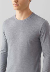 Maglietta a maniche lunghe, con collo rotondo, di colore grigio chiaro, realizzata in un tessuto liscio ed elastico con una delicata trama melangiata e vestibilità slim.