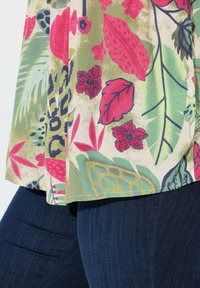 Gemusterter Blumestoff mit rosa Blumen und grünen Blättern auf einem hellen Hintergrund. Dunkelblaue Jeans sind darunter sichtbar.