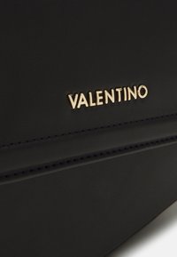 Svart läderhandväska med en gyllene "VALENTINO"-logotyp, slät textur, subtila sömmar och en elegant, rektangulär design.