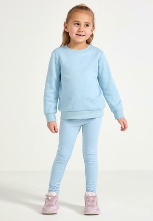 Ljusblå sweatshirt med ribbad mudd, kombinerad med matchande leggings. Materialet verkar mjukt och elastiskt. Bärs med rosa sneakers.