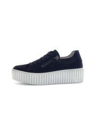 Zwarte suède sneaker met dikke witte geribbelde platformzool, vetersluiting aan de voorkant en een ritsdetail aan de zijkant op een witte achtergrond.