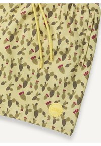 Tissu jaune avec un motif de cactus en vert et bordeaux, avec des cordons jaunes et un patch logo COUMAR rond jaune.